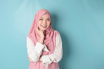 Fototapeta premium Portrait of a cheerful Muslim Asian woman standing and smiling at the camera, isolated on blue background