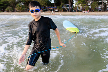 Young teen boy surfer holding rope of soft board, bring it to try again in wave. Rookie teenager surfboard student playing on water in strive focus action. - 526214270