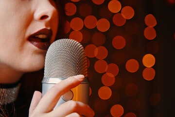Close-up of women's lips painted with burgundy lipstick and retro microphone. Female singer with disco mic on bokeh light background. Redhead girl starting concert. Copy space for gig posters.