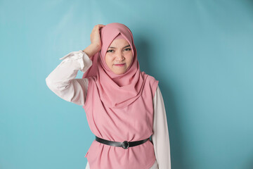 Fototapeta premium An Asian Muslim girl with a headache holds her head. Sullen young woman on a blue background copy space