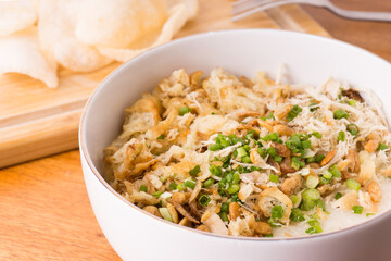 Close up view of Chicken congee or chicken porridge. Equipped with shredded chicken, cakwe or youtiao, garlic crackers, peanuts and spring onions