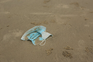 Surgical face mask and plastic bag leave as garbage on sea sand. Concept of environmental pollution impact form coronavirus covid 19 pandemic.