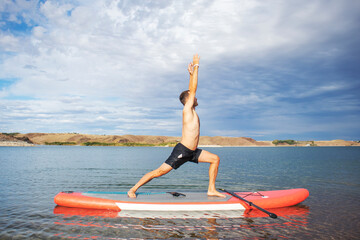 Virabhadrasana. a man does a war pose on a surfboard with a paddle