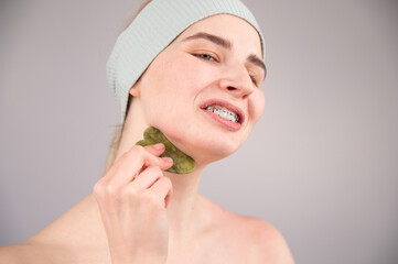 Portrait of a young woman massages her face with a gouache scraper on a white background.