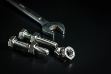 Bolts and nuts with wrench tool on a black background.