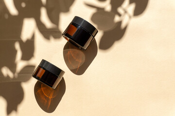 Two jars of amber glass for cosmetics on brown background with floral shadows. Unmarked mockups of...