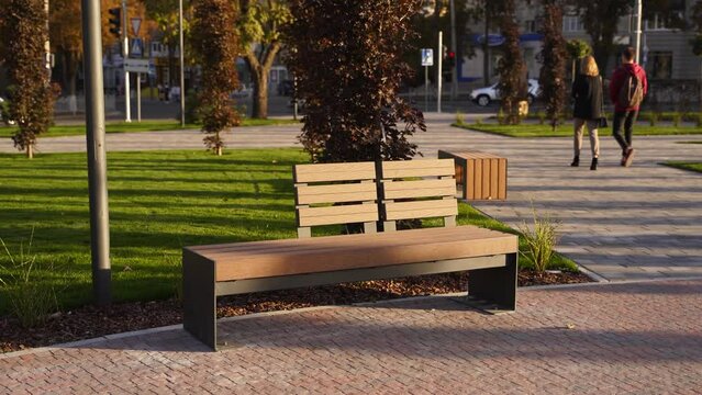 Modern wooden benches on the lawn in the park. Stylish new bench in city recreation area on sunrise or sunset. Urbanism theme public space landscape design. No people on empty street sidewalk.