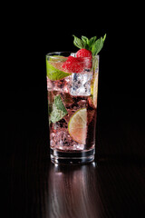 Ice drink with raspberries, lime wedges and mint on a black background. Selective focus.