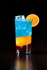 Multicolored blue lemonade cocktail with orange, red jam and ice. Side view, selective focus.