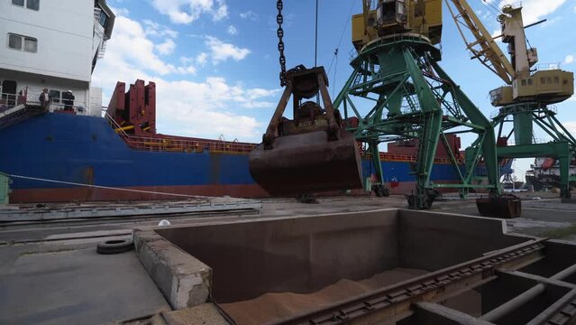 Grain transshipment from container to ship cargo holds with a double rope dual scoop clamshell grab on crane in sea port. Wheat shipment with water transport. Agricultural commodities transportation.