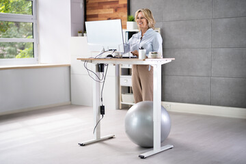 Woman Using Adjustable Height Standing Desk In Office