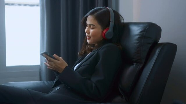 Young relaxing business woman using smartphone and listening to music in modern office.