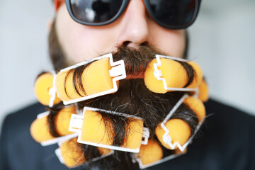 Cheerful hipster man with curlers in a beard. Surprised man with glasses looks in front.