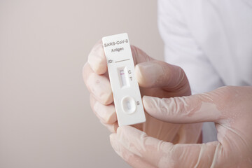 A doctor or nurse wearing rubber gloves holding a 1 red line Antigen Rapid Test kit (ATK) with negative results during a COVID-19 swab test.