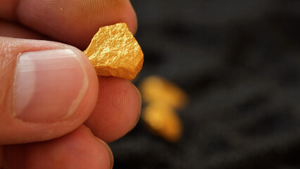 Mining man's hand holds a lump of pure gold from the mine and examines it on a black background.