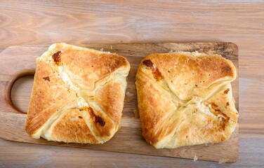 Homemade square shaped pies stuffed with cheese on a dark wooden board.