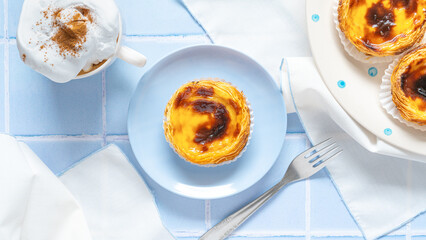 Traditional Portuguese egg tarts dessert Pasteis Pastel de nata or Pastels de Belem with a cup of capuchino coffee and forks on the blue tile. Flat lay