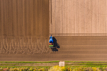 Aerial view of blue tractor plowing a field leaving tire tracks - Powered by Adobe