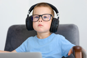 A boy in glasses and headphones listens in headphones while sitting 