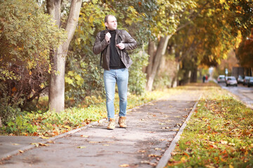 Autumn concept. A man walks through the city. Autumn leaves on the footpath. 