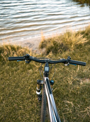 Fototapeta na wymiar Summer evening on the lake. Close-up of a bicycle handlebar in front of a river background. Countryside adventures at the sunset.