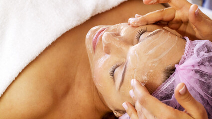Woman in a spa salon on cosmetic procedures for facial care. Cosmetologist applies  a cosmetic...