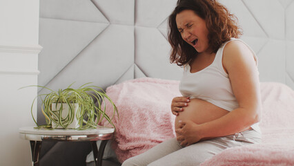 Expectant mother suffering from pregnant pain. Pregnant woman feeling ache lying on a bad. ...