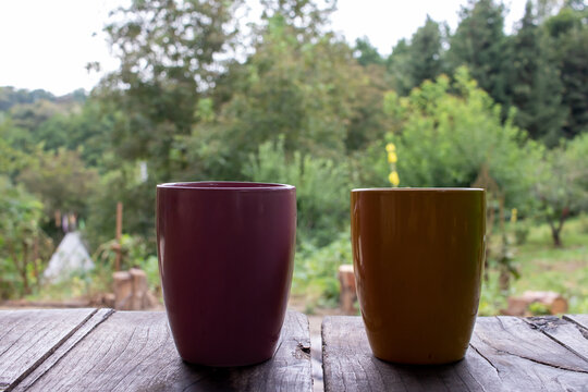 Cup Of Tea Or Coffee On The Table Outdoors. Two Colorful Mugs On Wooden Table In Summer, Autumn Forest Landscape Nature Background. Vacation, Travel, Picnic, Stress Relief, Camping Concept