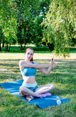 beautiful young woman does sports fitness or yoga on mat in park on outdoor on sunny summer day, healthy lifestyle, training and stretching in open air
