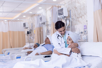 Smiling girl lying on bed embracing doctor during visit at hospital ward
