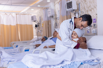 Smiling girl lying on bed embracing doctor during visit at hospital ward
