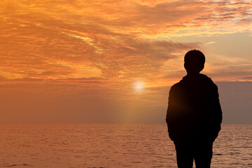 a man standing in front of sunset over the sea with warm sky. Looking for passion or future....