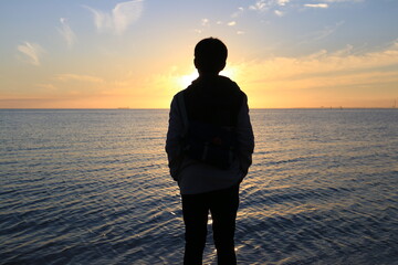 a man stand in front of sunset over the sea with warm blue sky. Looking for passion or future. thinking of life.  - Powered by Adobe