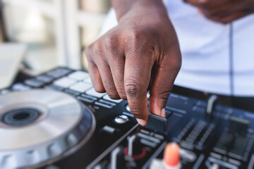 View of Dj mixer and vinyl plate with headphones on a table with african american DJ playing on stage and mixes the track in the background, during summer open air event techno party, hand close up