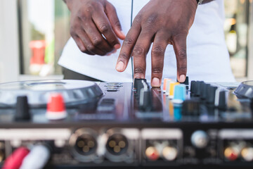 View of Dj mixer and vinyl plate with headphones on a table with african american DJ playing on stage and mixes the track in the background, during summer open air event techno party, hand close up