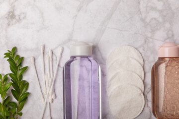 Micellar water, makeup remover wipes, cotton swabs and flowers. Cleansing the skin of sebum and makeup. Composition on a white marble background. Beauty concept. Copy space text. flat lay