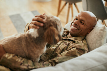 Happy African American military man enjoys with his dog at home.