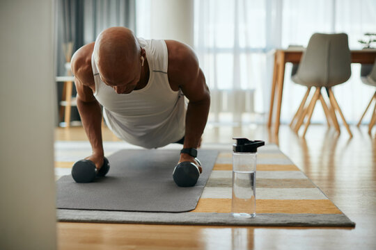 African American athlete using hand weights while exercising push-ups at home.