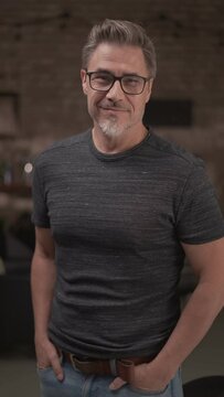 Portrait of happy middle aged man in a dark industrial room wearing glasses, smiling.