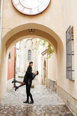 Stylish couple in the yard of the old town. The guy lifts the girl up, November 2, 2019, Lviv, Ukraine.