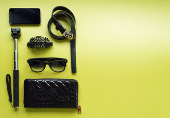 make up bag with cosmetics and brushes, smart-phone, selfie stick on green background. top view....