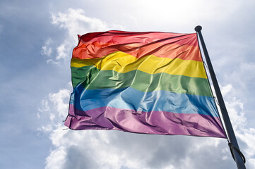 LGBTIQ flag waving on the wind on flagpole in town. A symbol of the LGBT community and social movements. Symbol of lesbian, gay, bisexual, transgender
