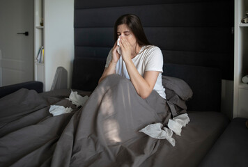Woman lying in bed during an illness suffering from nasal congestion or holds napkin tissue near...