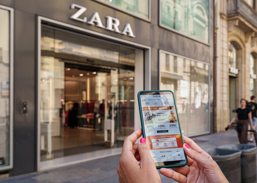 Woman holding a smartphone with the Shein app on the screen and a Zara store in the background