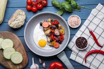 Flat lay composition with delicious cooked egg and vegetables in frying pan on blue table