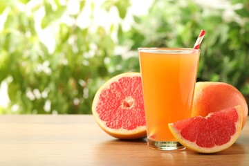 Glass of delicious grapefruit juice on wooden table against blurred background, space for text