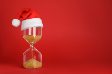 Hourglass and Santa hat on red background, space for text. Christmas countdown
