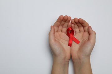 Little girl holding red ribbon on white background, top view. AIDS disease awareness