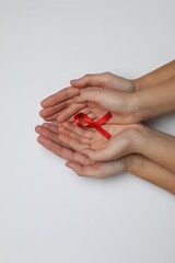 Woman and girl holding red ribbon on white background, top view. AIDS disease awareness
