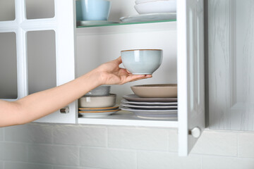 Woman taking ceramic bowl from cabinet at home, closeup
